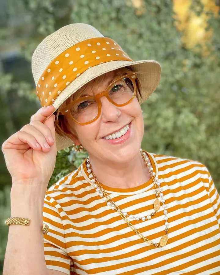Noémie en chapeau et lunettes, pull rayé orange