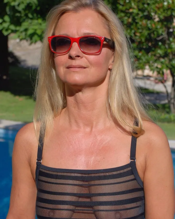 Femme blonde aux yeux marrons en maillot de bain noir transparent, posant près d'une piscine