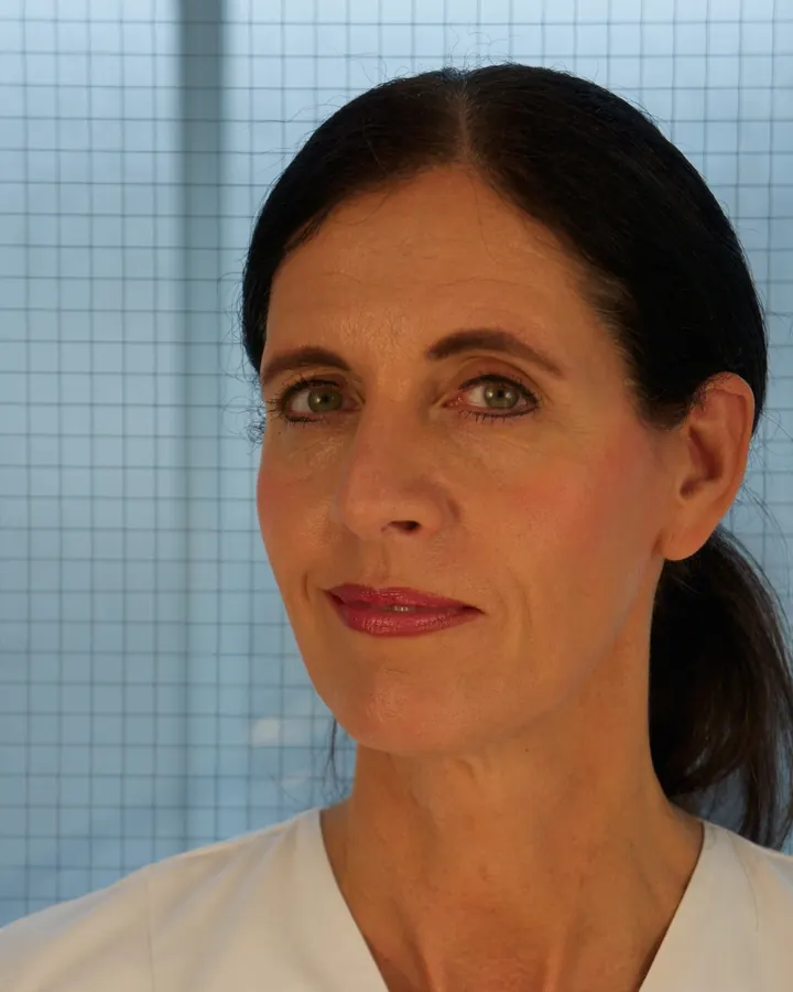 Femme brune aux yeux gris en chemise blanche, posant dans un bureau