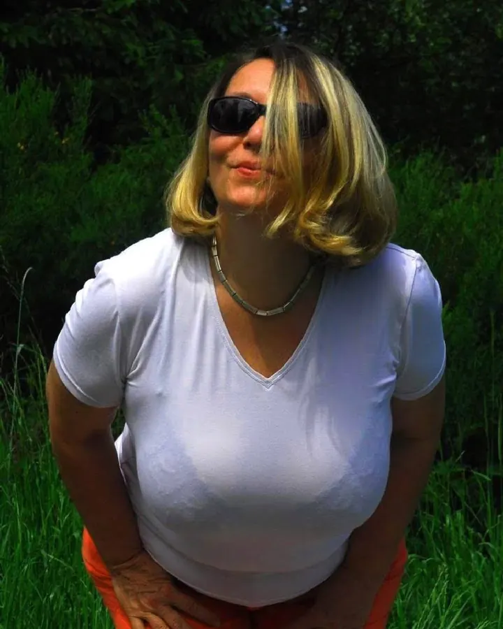 Femme aux cheveux blonds, portant une robe noire, assise sur un canapé noir.