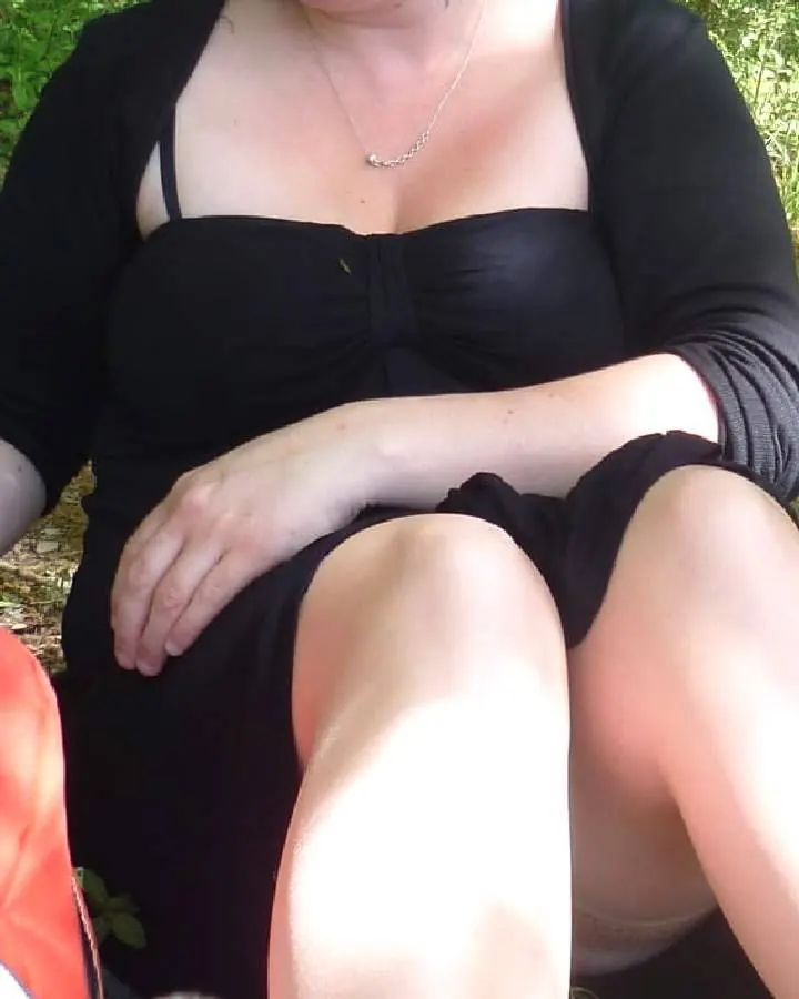 Femme aux cheveux bruns foncés, portant une robe noire, assise sur un banc en extérieur.