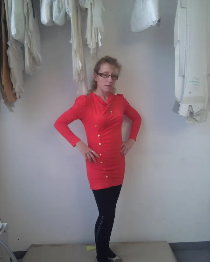 Femme blonde portant une robe marron, assise sur un escalier, les mains sur les barrières, portant des collants noirs et des bottes noires, dans un couloir avec tapis rouge.