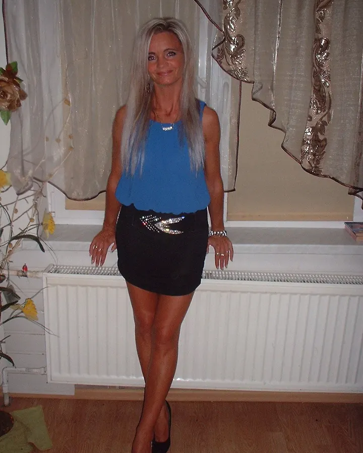 Femme blonde en haut bleu, jupe noire, souriante