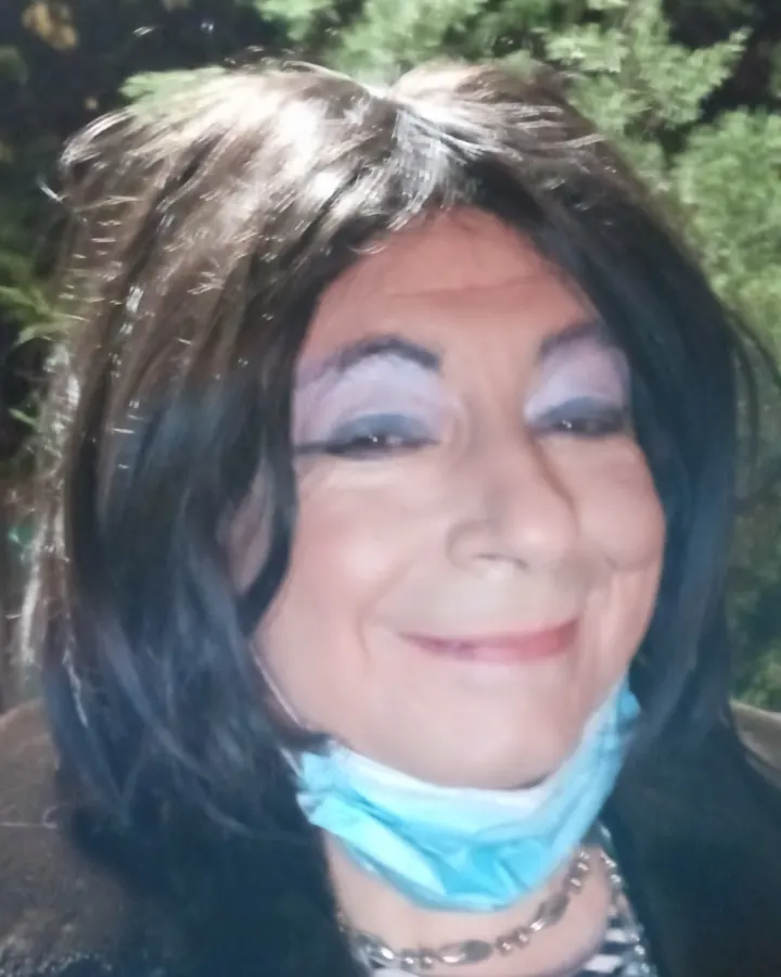 Femme aux cheveux noirs courts, souriante, en chemisier rayé bleu-blanc, avec masque bleu autour du cou